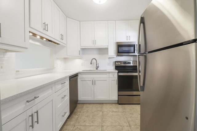 kitchen featuring stainless steel appliances, a sink, white cabinetry, backsplash, and light stone countertops