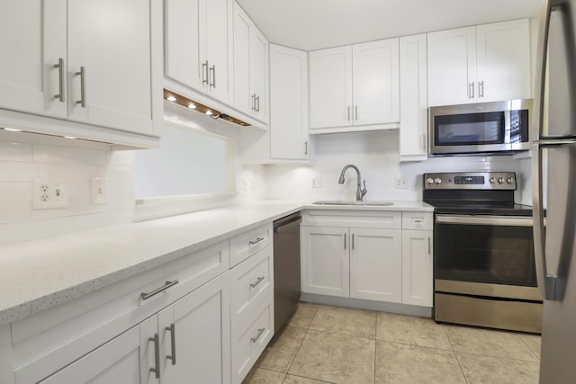 kitchen with stainless steel appliances, a sink, white cabinets, decorative backsplash, and light stone counters