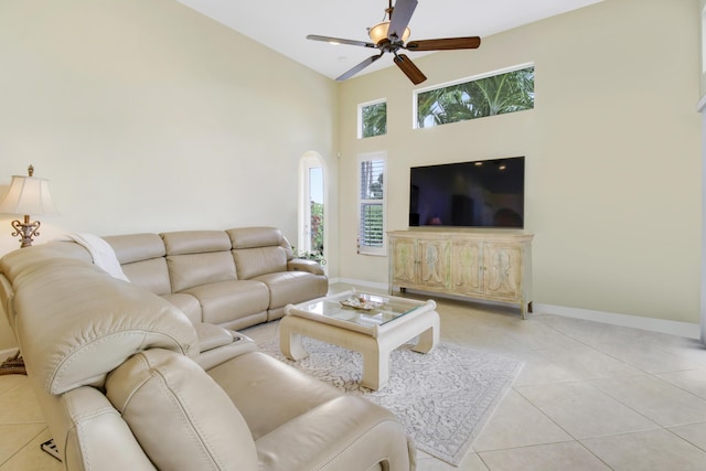 living area featuring ceiling fan, baseboards, light tile patterned floors, and a towering ceiling