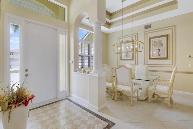 tiled entrance foyer with decorative columns, arched walkways, ornamental molding, baseboards, and a chandelier