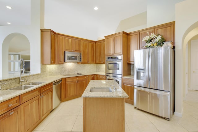 kitchen featuring appliances with stainless steel finishes, a sink, arched walkways, light stone countertops, and decorative backsplash
