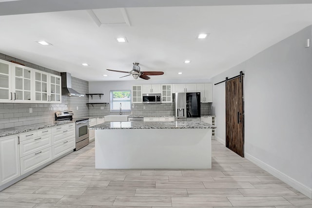 kitchen featuring stainless steel appliances, wall chimney range hood, a center island, tasteful backsplash, and a ceiling fan