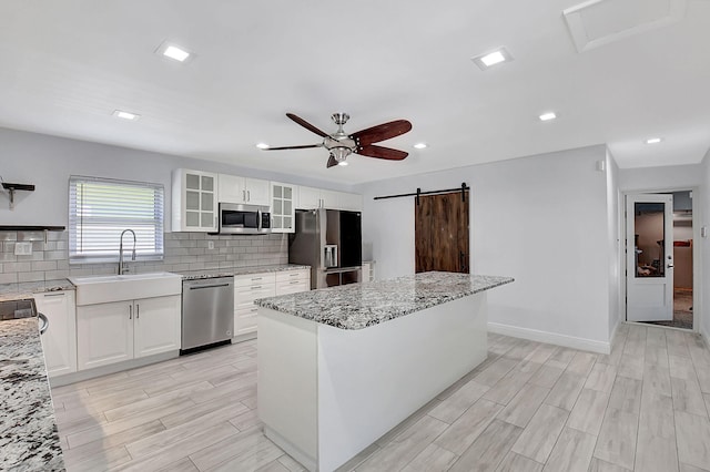 kitchen featuring appliances with stainless steel finishes, a sink, ceiling fan, tasteful backsplash, and a center island
