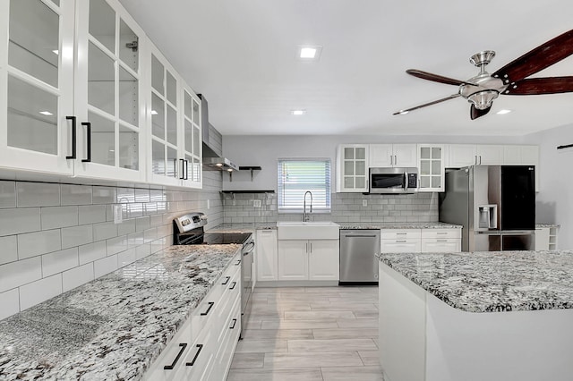 kitchen featuring stainless steel appliances, a sink, tasteful backsplash, light stone countertops, and glass insert cabinets