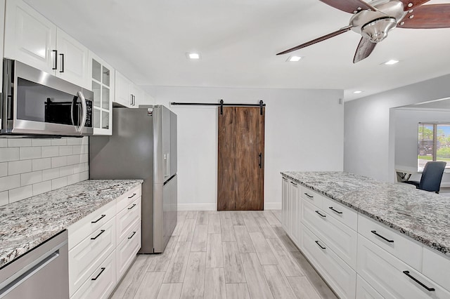 kitchen featuring appliances with stainless steel finishes, a barn door, a ceiling fan, glass insert cabinets, and backsplash