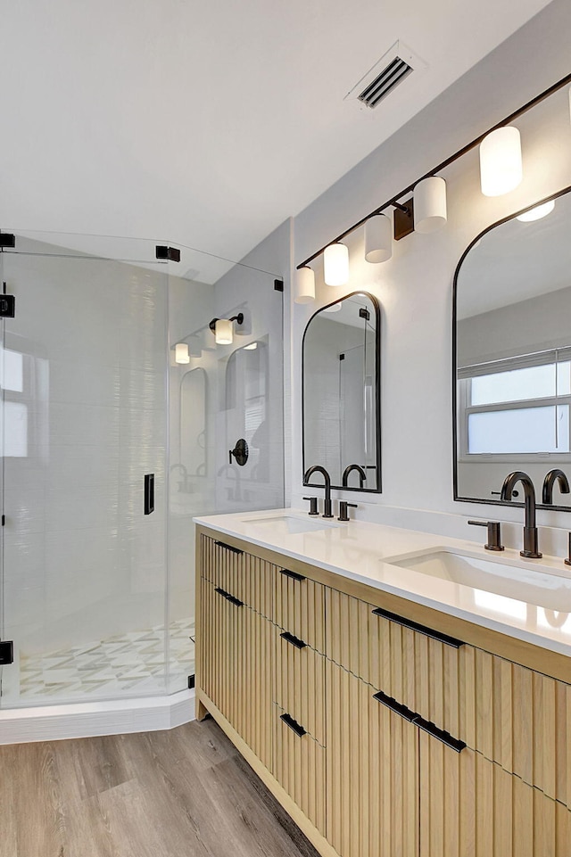 full bathroom featuring wood finished floors, a shower stall, and double vanity