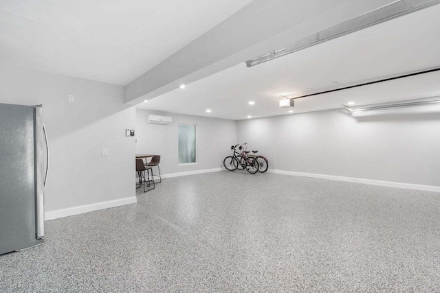 garage with freestanding refrigerator, an AC wall unit, baseboards, and recessed lighting