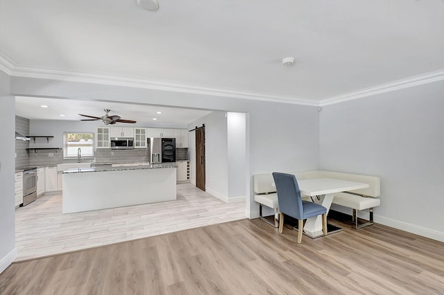 kitchen featuring stainless steel appliances, a barn door, light wood-type flooring, white cabinetry, and decorative backsplash