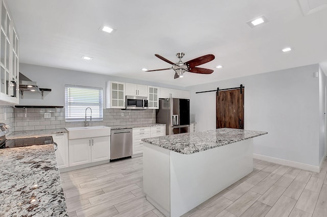kitchen with appliances with stainless steel finishes, a sink, a barn door, ceiling fan, and decorative backsplash