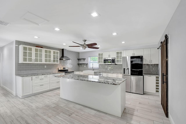 kitchen featuring appliances with stainless steel finishes, wall chimney exhaust hood, tasteful backsplash, wood finish floors, and baseboards