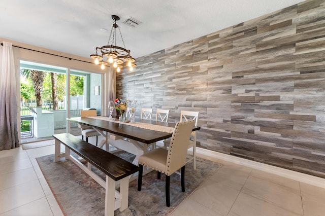 dining space featuring an accent wall, light tile patterned flooring, a chandelier, and wooden walls