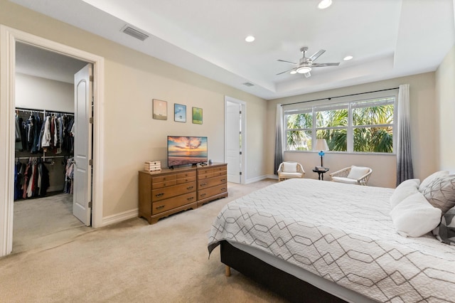 bedroom featuring baseboards, light carpet, a walk in closet, a raised ceiling, and recessed lighting