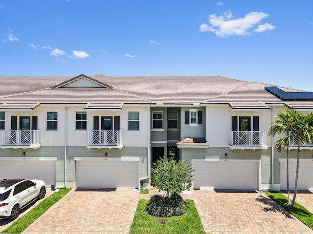 townhome / multi-family property with a garage, driveway, stucco siding, and a tiled roof
