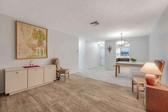 living area featuring a textured ceiling, light wood finished floors, baseboards, and a chandelier
