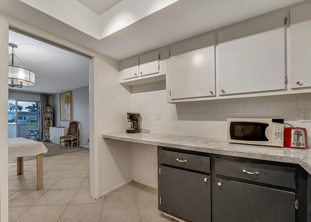 kitchen with white microwave, backsplash, white cabinets, light tile patterned flooring, and baseboards