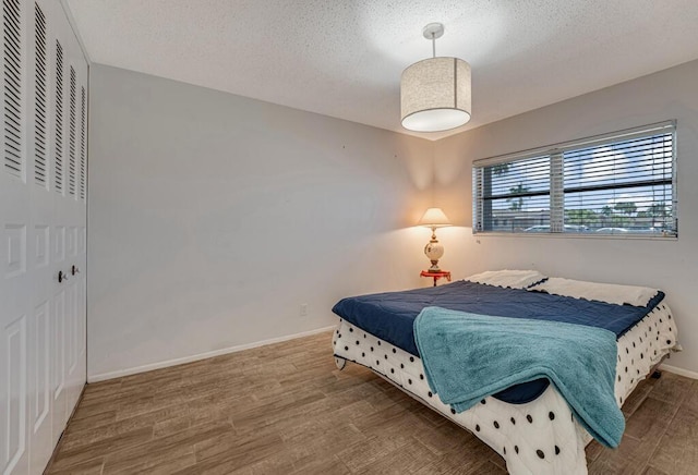 bedroom featuring wood finished floors, a textured ceiling, baseboards, and a closet