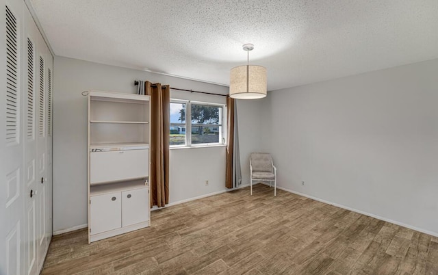 unfurnished bedroom with a textured ceiling, wood finished floors, baseboards, and a closet