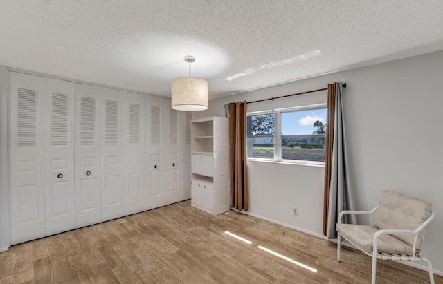 unfurnished bedroom with wood finished floors, a textured ceiling, a closet, and baseboards