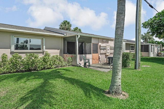 back of house with a yard, stucco siding, and a sunroom
