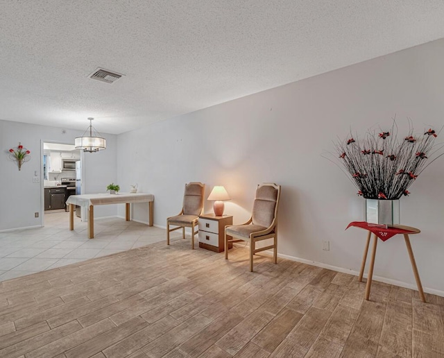 living area with light wood-style flooring, a textured ceiling, a chandelier, and baseboards