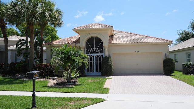mediterranean / spanish house with an attached garage, a tiled roof, decorative driveway, stucco siding, and a front lawn