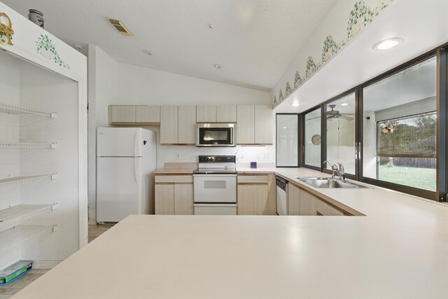 kitchen featuring white appliances, a sink, light countertops, lofted ceiling, and light brown cabinetry