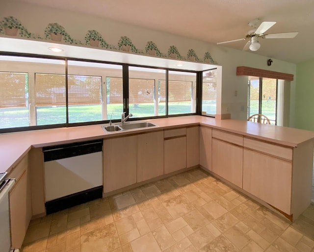 kitchen featuring white dishwasher, a sink, light countertops, light stone finish flooring, and a peninsula