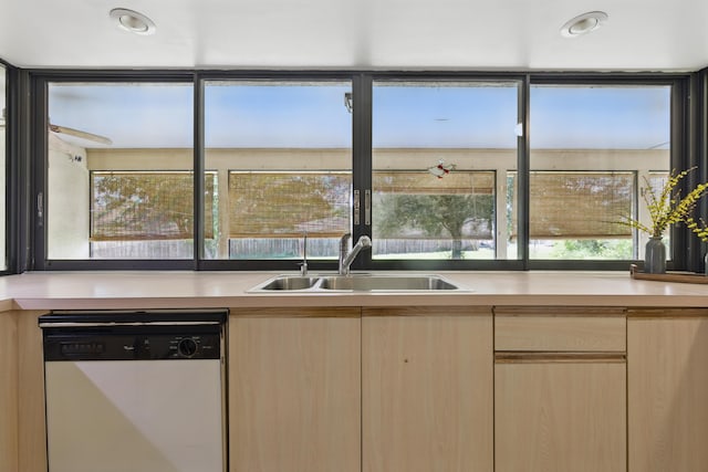 kitchen with white dishwasher, light brown cabinets, a sink, and light countertops