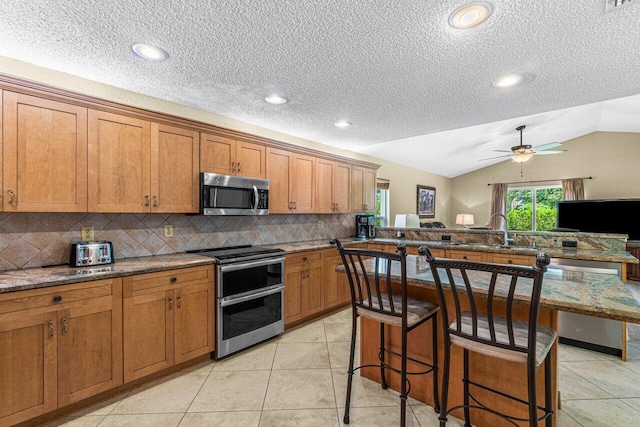 22075 Flower Dr, Boca Raton, FL 33428 - kitchen with stainless steel appliances, a sink, brown cabinetry, tasteful backsplash, and a breakfast bar