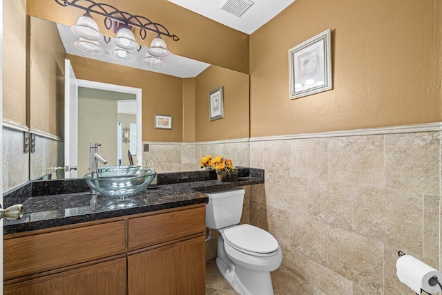 22075 Flower Dr, Boca Raton, FL 33428 - half bath with tile walls, toilet, vanity, a wainscoted wall, and tile patterned flooring