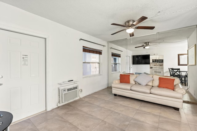 living room featuring ceiling fan, an AC wall unit, light tile patterned floors, and a textured ceiling