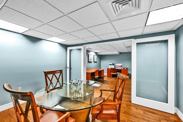 dining area featuring wood finished floors, a paneled ceiling, and baseboards