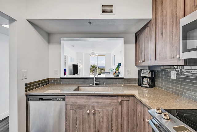 kitchen with appliances with stainless steel finishes, a sink, decorative backsplash, ceiling fan, and brown cabinetry
