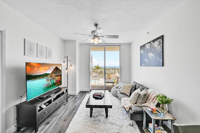 living area with wood finished floors, a ceiling fan, baseboards, and a textured ceiling