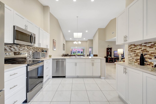 kitchen featuring stainless steel appliances, a sink, a peninsula, a chandelier, and backsplash