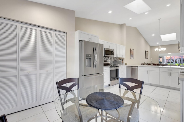 kitchen featuring appliances with stainless steel finishes, a skylight, light tile patterned floors, a chandelier, and white cabinets