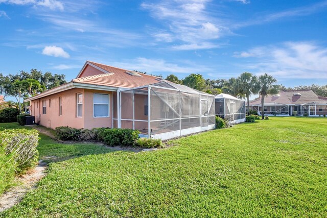 back of house featuring a yard, a tile roof, stucco siding, and glass enclosure