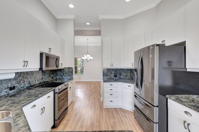 kitchen with appliances with stainless steel finishes, a chandelier, light wood-style floors, dark stone countertops, and crown molding