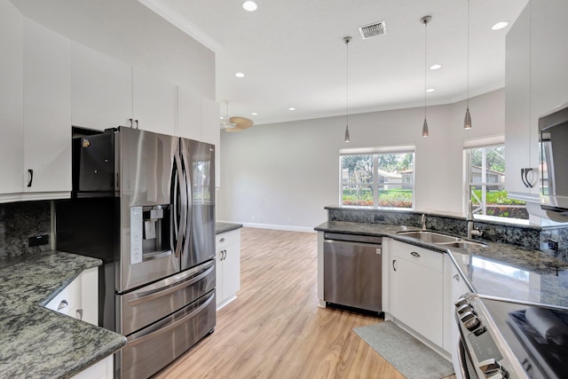 kitchen with appliances with stainless steel finishes, a sink, light wood finished floors, white cabinetry, and crown molding