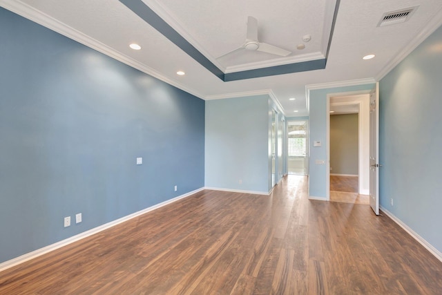 unfurnished room with a tray ceiling, dark wood finished floors, crown molding, baseboards, and recessed lighting