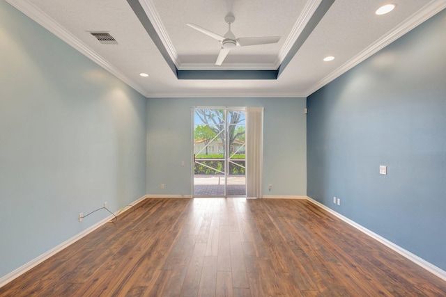 empty room with a raised ceiling, hardwood / wood-style flooring, crown molding, ceiling fan, and baseboards