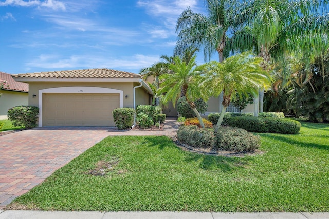 view of front of house with decorative driveway, an attached garage, a front yard, stucco siding, and a tile roof