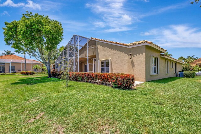 view of side of property with stucco siding, a lawn, and a lanai