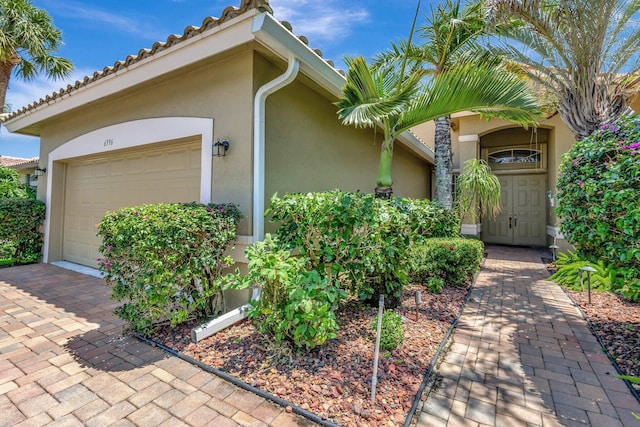 view of exterior entry featuring stucco siding, an attached garage, and driveway