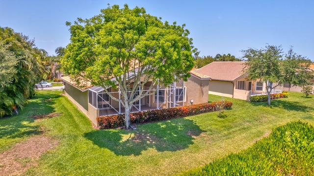 rear view of property with a lawn, stucco siding, and glass enclosure