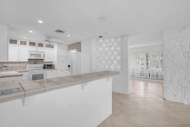 2230 NE 62nd St, Fort Lauderdale, FL 33308 - kitchen with white appliances, tile countertops, glass insert cabinets, ceiling fan, and white cabinetry
