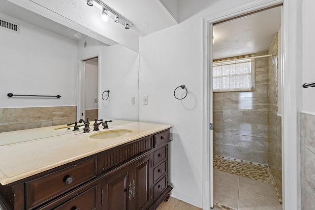 full bath with a tile shower, tile patterned flooring, and vanity