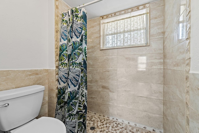 bathroom with tile walls, tiled shower, toilet, and wainscoting
