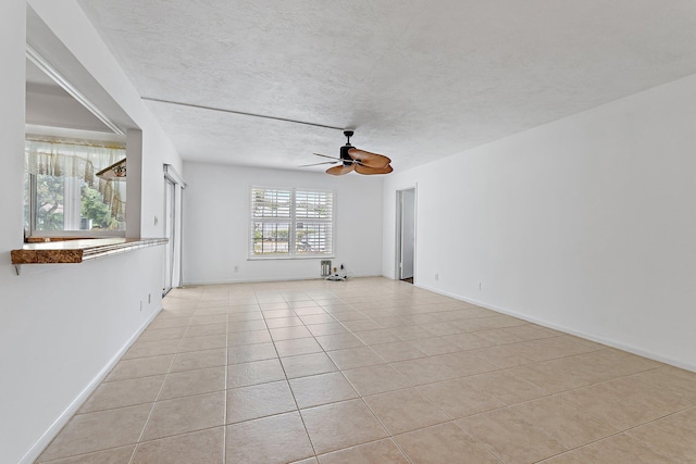 empty room featuring a ceiling fan, light tile patterned floors, a textured ceiling, and baseboards