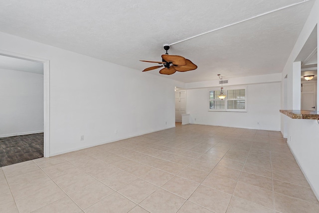 empty room featuring a ceiling fan, light tile patterned flooring, a textured ceiling, and baseboards
